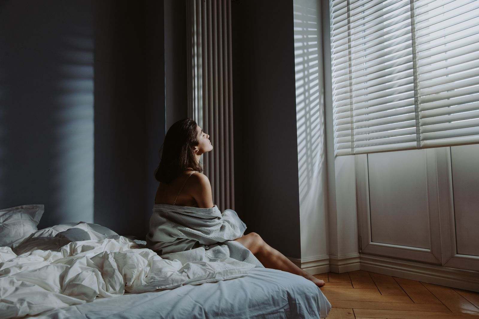 A woman sitting on the edge of a bed in soft window light