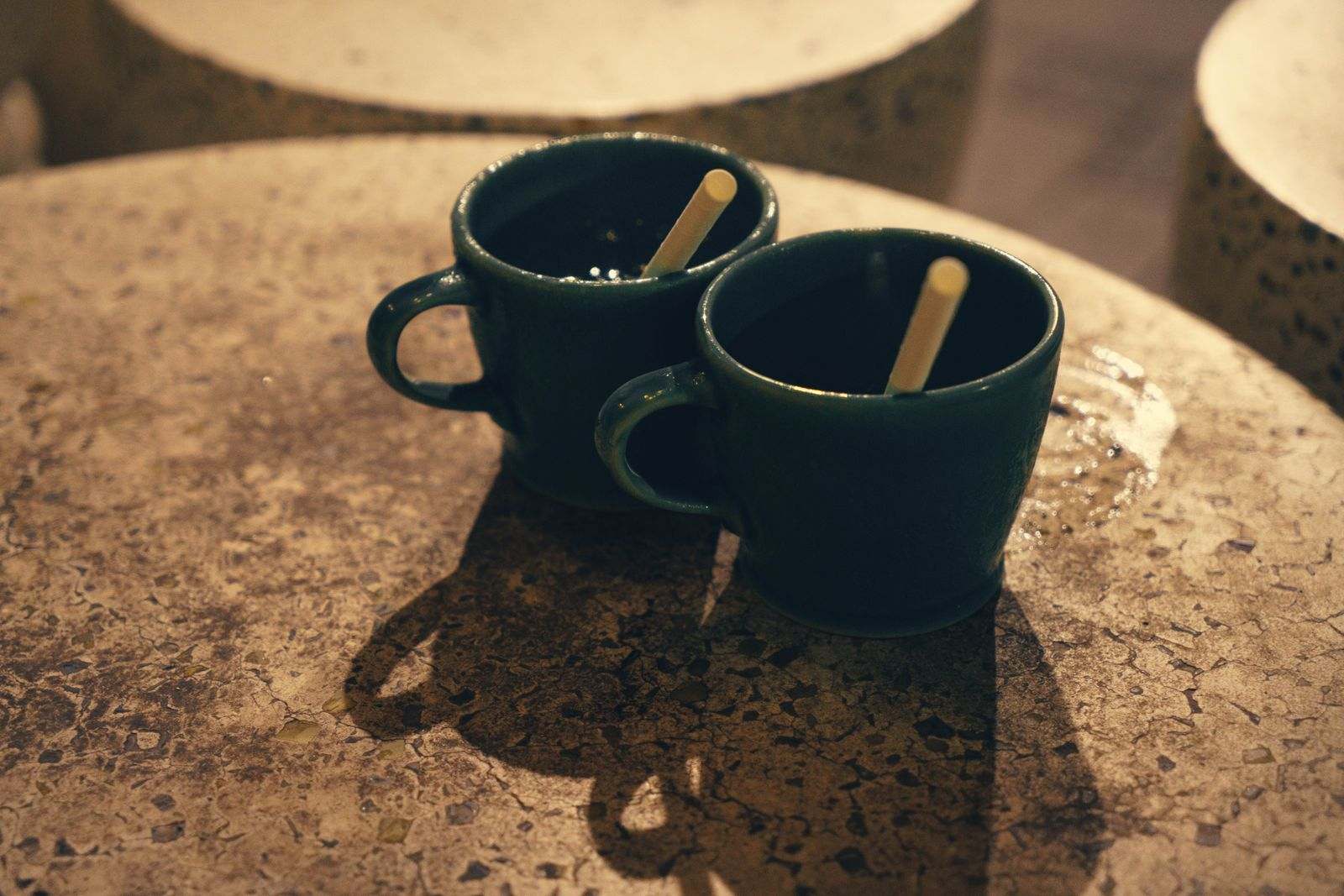 Two green mugs standing close together on a stone table