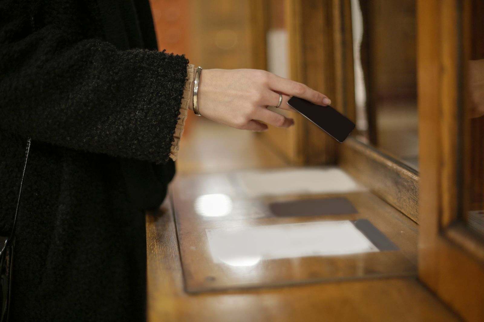 A hand paying with a bank card at a warm wooden counter