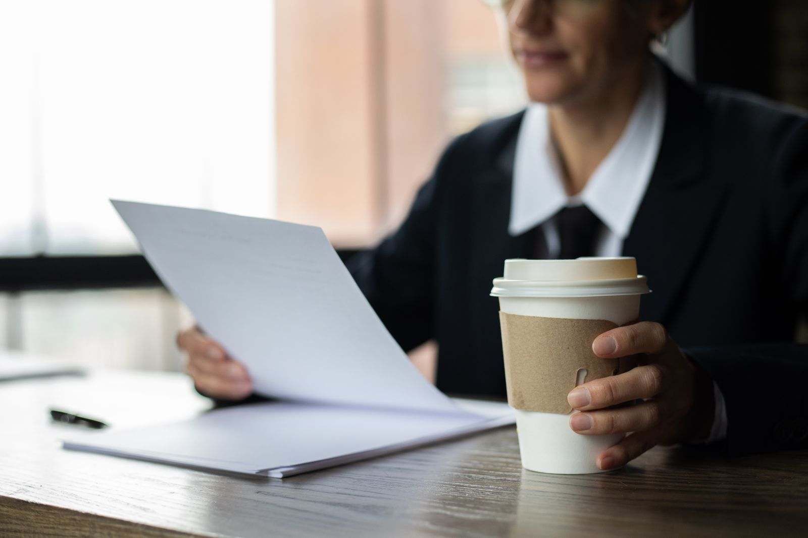 A person reading a stack of printed pages with a coffee at a desk