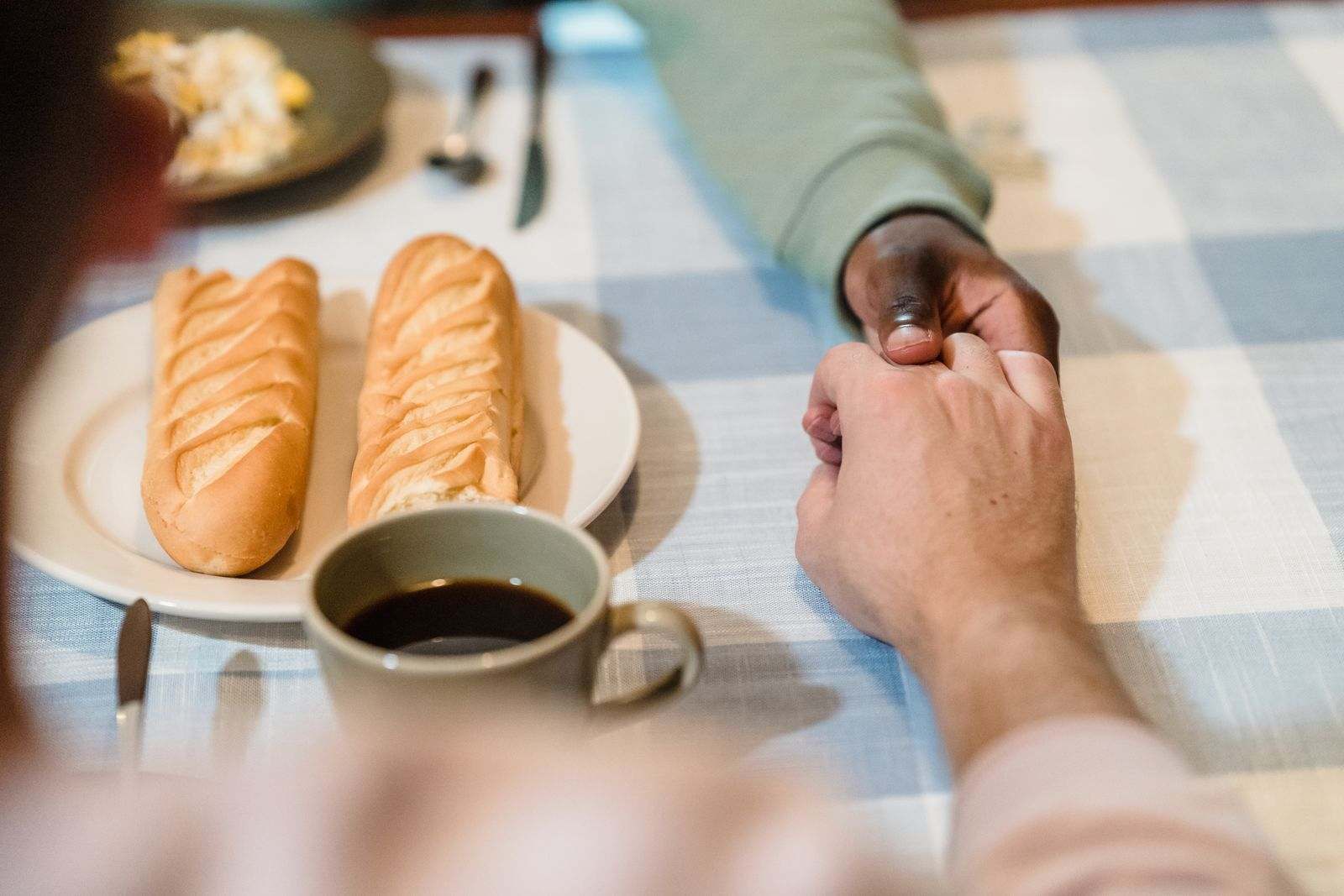 A couple holding hands across a breakfast table with bread and coffee
