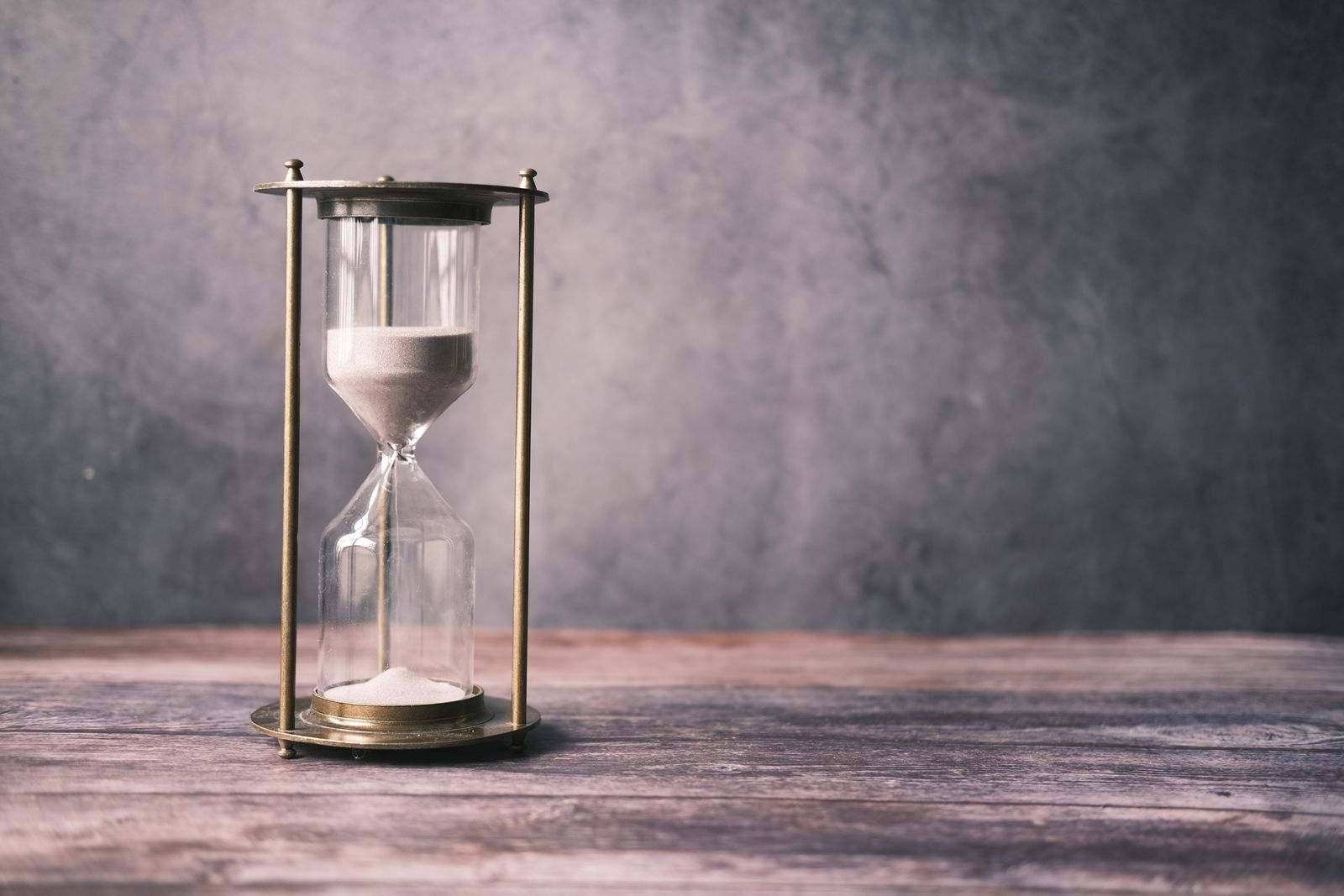 An hourglass with the sand running, on a wooden table
