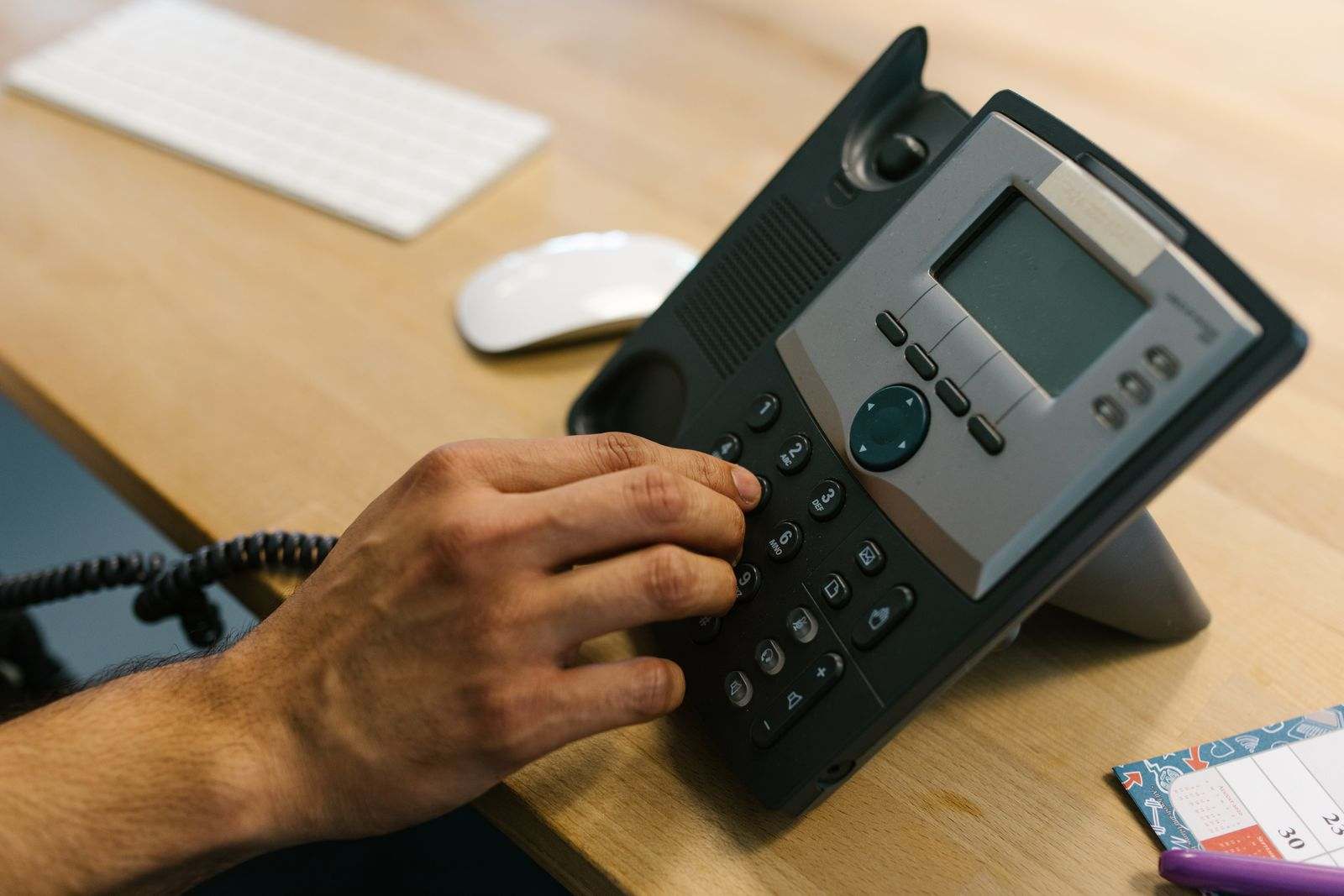 A hand dialing a number on a desk phone keypad
