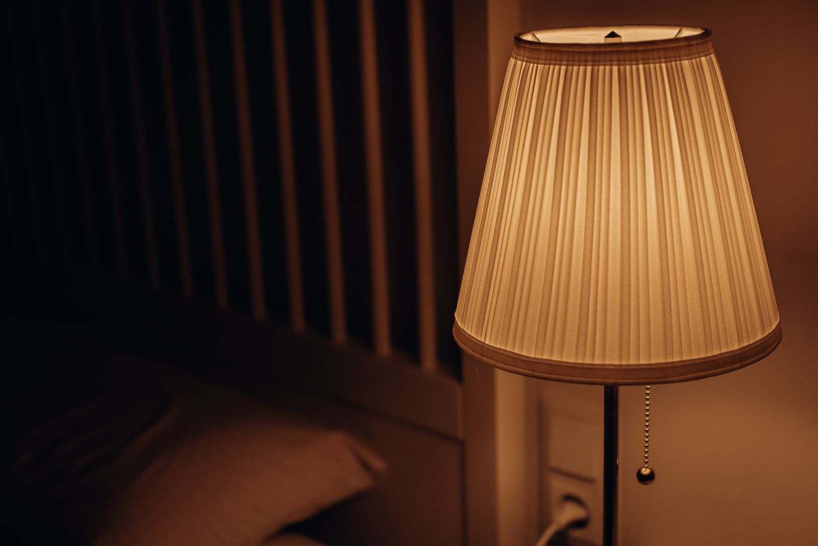 A warm bedside lamp glowing next to a bed at night