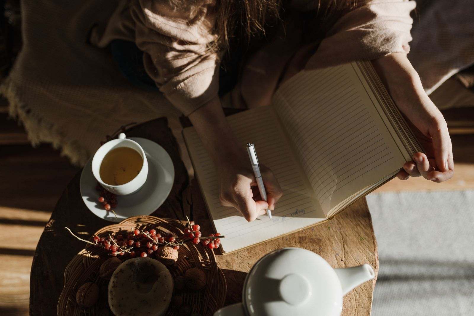 A person writing in a notebook beside a cup of tea