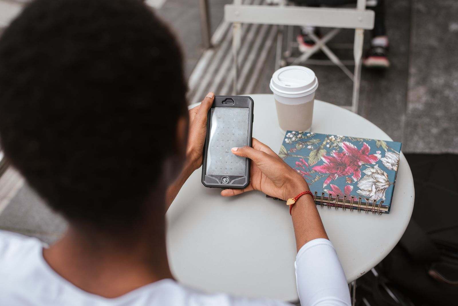 A person checking a message on a phone beside a notebook and coffee