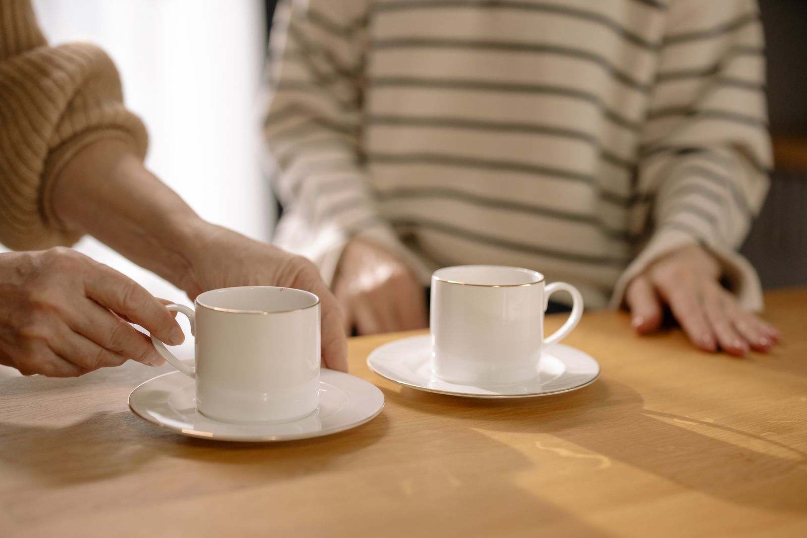 Two people sitting at a wooden table with two white cups of coffee