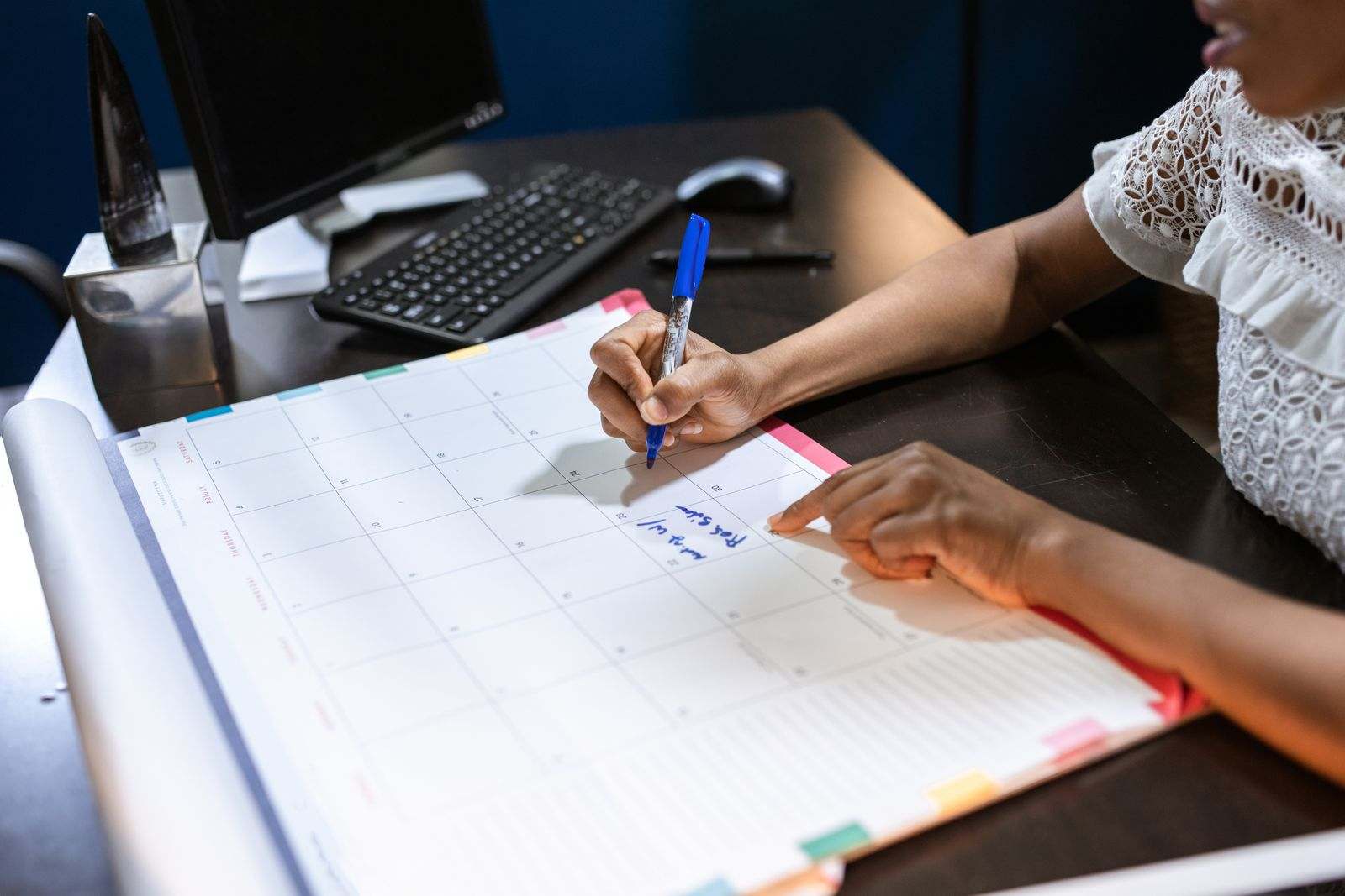 A hand writing a note on a large desk calendar