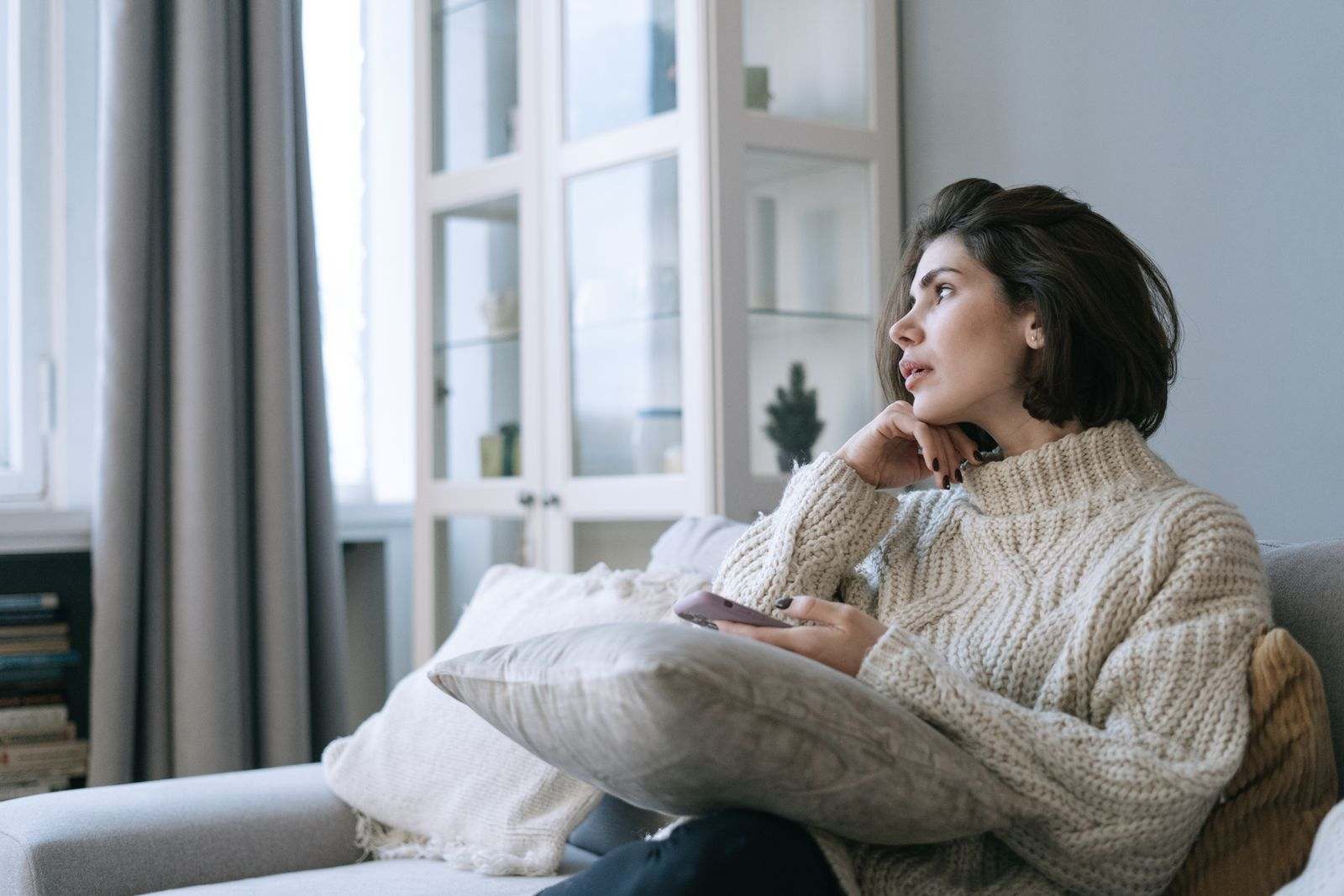 A woman on a couch holding her phone, looking out the window